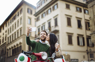 Mann macht Selfie mit Freundin, die ihn auf die Wangen küsst, in Florenz, Italien - SODF00752