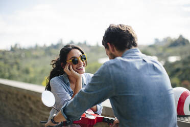 Glückliche Frau mit Sonnenbrille im Gespräch mit ihrem Freund auf einer Vespa sitzend - SODF00760
