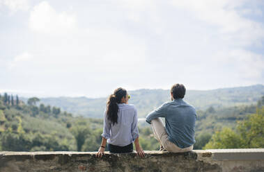 Couple looking at view while sitting on retaining wall against sky during sunny day - SODF00762