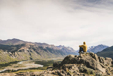 Männlicher Wanderer betrachtet die Aussicht, während er auf einem Felsen gegen den Himmel sitzt, Patagonien, Argentinien - UUF20672