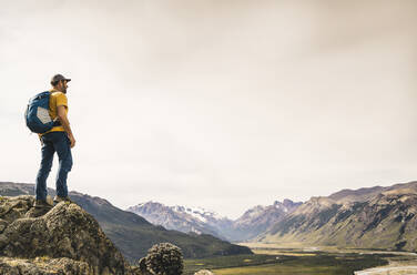Male hiker with backpack standing on rock against sky at Patagonia, Argentina - UUF20674