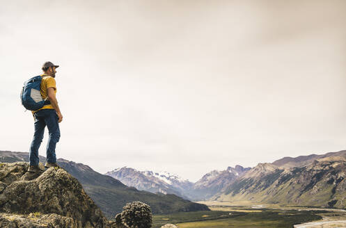 Männlicher Wanderer mit Rucksack auf einem Felsen stehend gegen den Himmel in Patagonien, Argentinien - UUF20674