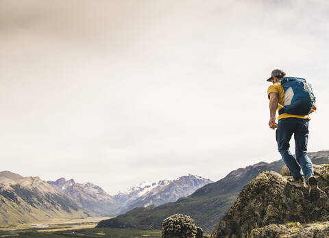 Älterer Wanderer mit Rucksack, der auf einem Felsen gegen den Himmel läuft, Patagonien, Argentinien, lizenzfreies Stockfoto