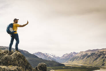 Älterer Mann, der ein Selfie mit seinem Smartphone macht, während er auf einem Felsen gegen den Himmel steht, Patagonien, Argentinien - UUF20679