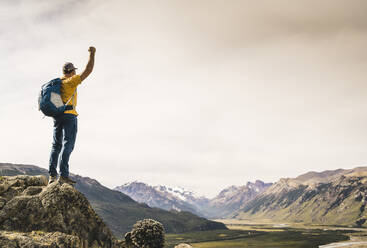 Man with arm raised looking at mountains while standing on rock, Patagonia, Argentina - UUF20680