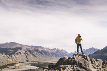 Älterer Mann spricht über Smartphone, während er auf einem Felsen gegen den Himmel steht, Patagonien, Argentinien - UUF20687