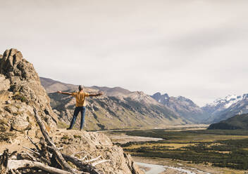 Male hiker with arms outstretched looking at Patagonia Andes while standing on rock, Argentina - UUF20690