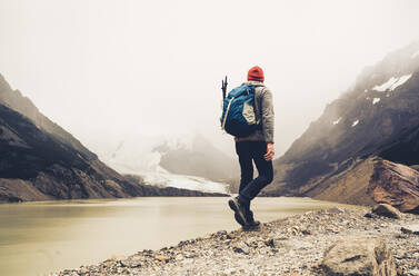 Mature man with backpack walking by lake against sky, Patagonia, Argentina - UUF20697