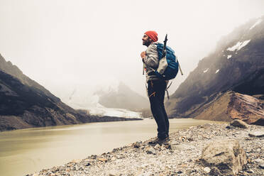 Älterer Mann mit Rucksack steht am See gegen den Himmel in Patagonien, Argentinien - UUF20698