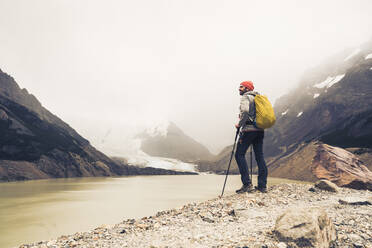 Man with hiking poles standing by lake against sky at Patagonia, Argentina - UUF20700