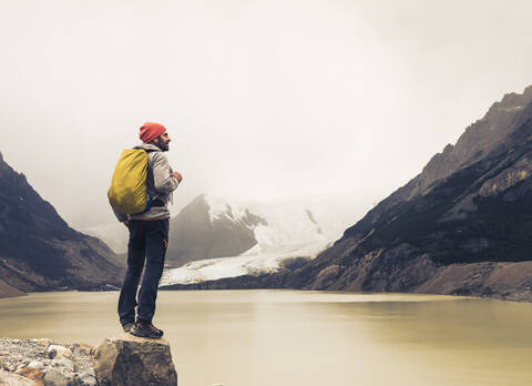 Älterer Mann mit Rucksack steht auf einem Felsen am See in Patagonien, Argentinien, lizenzfreies Stockfoto
