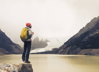 Älterer Mann mit Rucksack steht auf einem Felsen am See in Patagonien, Argentinien - UUF20702