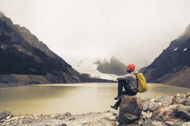 Älterer Mann mit Rucksack sitzt auf einem Felsen am See in Patagonien, Argentinien - UUF20703