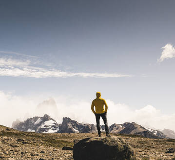 Männlicher Wanderer, der die Landschaft gegen den Himmel betrachtet, während er auf einem Felsen steht, Patagonien, Argentinien - UUF20708