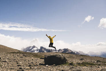 Unbekümmerter reifer Mann, der auf einem Felsen gegen den Himmel springt, Patagonien, Argentinien - UUF20710