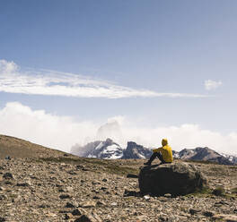 Männlicher Wanderer, der die Landschaft gegen den Himmel betrachtet, während er auf einem Felsen sitzt, Patagonien, Argentinien - UUF20711