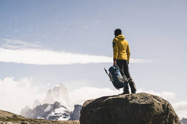 Männlicher Wanderer mit Rucksack auf einem Felsen stehend gegen den Himmel, Patagonien, Argentinien - UUF20713