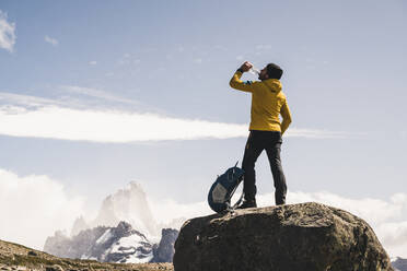 Männlicher Wanderer trinkt Wasser, während er auf einem Felsen gegen den Himmel steht, Patagonien, Argentinien - UUF20714