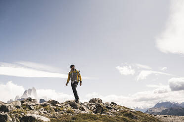 Älterer Mann mit Rucksack, der an einem sonnigen Tag auf einem Berg gegen den Himmel läuft, Patagonien, Argentinien - UUF20715