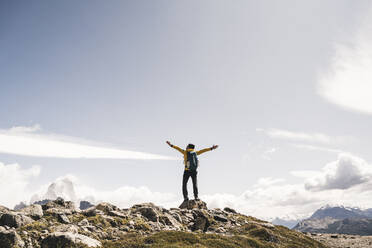 Man with arms outstretched standing on mountain against sky during sunny day, Patagonia, Argentina - UUF20719