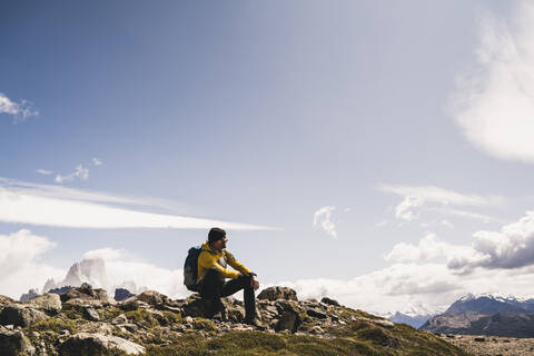 Männlicher Wanderer auf einem Berg sitzend gegen den Himmel an einem sonnigen Tag, Patagonien, Argentinien, lizenzfreies Stockfoto