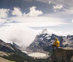 Man looking at snowcapped mountain while sitting on rock against sky, Patagonia, Argentina - UUF20724