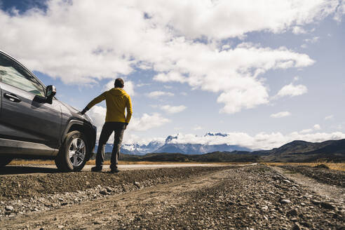 Älterer Mann steht neben einem Auto auf einer unbefestigten Straße im Torres Del Paine National Park, Patagonien, Chile - UUF20730