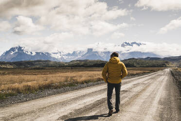 Älterer Mann, der auf einer unbefestigten Straße gegen den bewölkten Himmel läuft, Torres Del Paine National Park, Patagonien, Chile - UUF20731