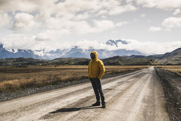 Male hiker standing on dirt road against sky at Torres Del Paine National Park, Patagonia, Chile - UUF20735