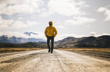 Männlicher Wanderer mit den Händen in den Taschen, der auf einer unbefestigten Straße im Torres Del Paine National Park, Patagonien, Chile, wandert - UUF20738