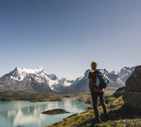 Mann mit Rucksack schaut auf einen See gegen den klaren Himmel, Torres Del Paine National Park, Patagonien, Chile - UUF20746