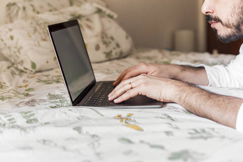 Mann mit Laptop auf dem Bett, lizenzfreies Stockfoto