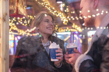 Nahaufnahme eines glücklichen Paares mit heißer Schokolade im Gespräch in einem Geschäft, gesehen durch ein Fenster - WPEF03101