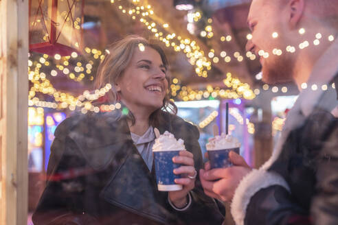 Close-up of happy couple with hot chocolates talking in store seen through window - WPEF03101