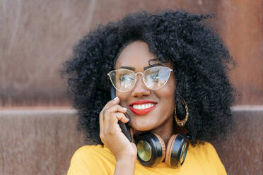 Porträt einer lächelnden Frau mit Afro-Haar, die ein Smartphone benutzt - JAF00008