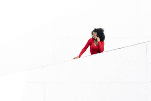 Young woman with afro hair using smartphone on white ramp - JAF00009