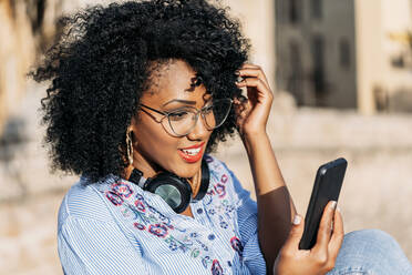 Lächelnde Frau mit Afro-Haar und Brille während eines Videoanrufs im Freien - JAF00011