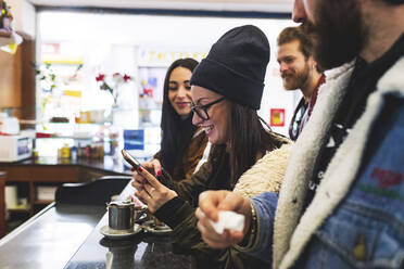 Lächelnde Frau, die ein Smartphone benutzt, während sie sich mit Freunden in einem Café amüsiert - MEUF00989