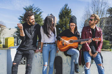 Mid adult woman playing guitar while enjoying with friends in city - MEUF00994