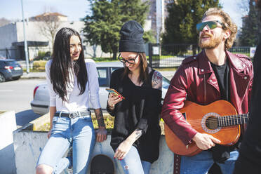 Bärtiger Mann spielt Gitarre, während er mit Freundinnen in der Stadt steht - MEUF00997