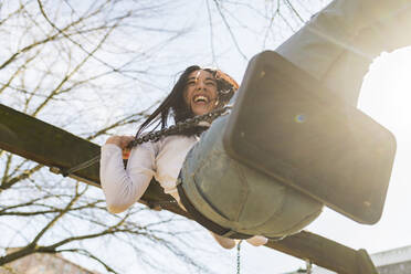 Fröhliche junge Frau schwingt gegen den Himmel im Park an einem sonnigen Tag - MEUF01013