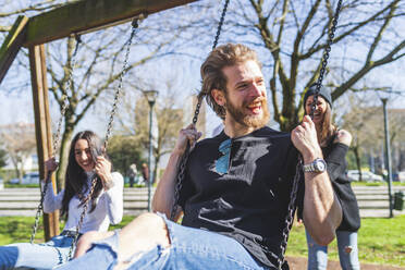 Fröhliche Freunde schaukeln im Park an einem sonnigen Tag - MEUF01014