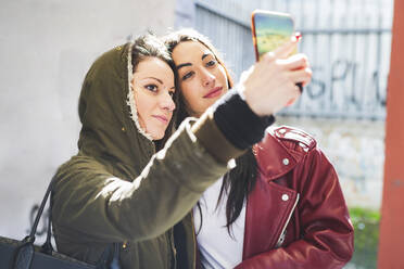 Frau, die ein Selfie mit ihrer Freundin macht, während sie in der Stadt an der Wand steht - MEUF01027