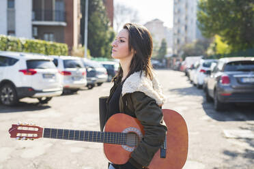 Mid adult woman carrying guitar while walking on road in city - MEUF01033