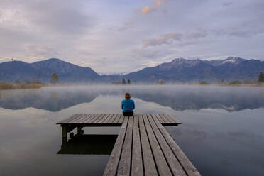 Germany, Bavaria, Schlehdorf, Woman sitting at end of jetty admiring Eichsee at foggy dawn - LBF03091