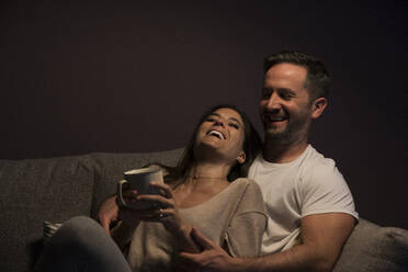 Happy loving couple relaxing on sofa against wall at home - MTBF00460