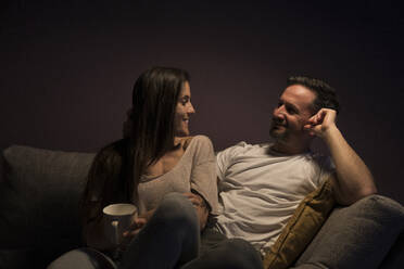 Glückliches Paar, das sich gegenseitig ansieht, während es sich auf dem Sofa zu Hause entspannt - MTBF00462