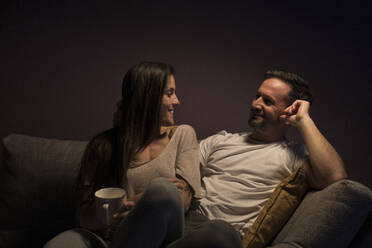 Happy couple looking at each other while relaxing on sofa at home - MTBF00462