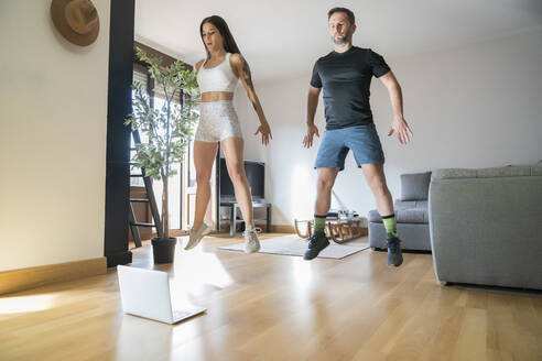 Couple jumping while exercising on hardwood floor at home - MTBF00476