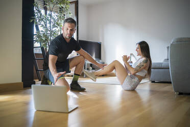 Mann trainiert mit Frau, während er im Wohnzimmer auf den Laptop schaut - MTBF00477